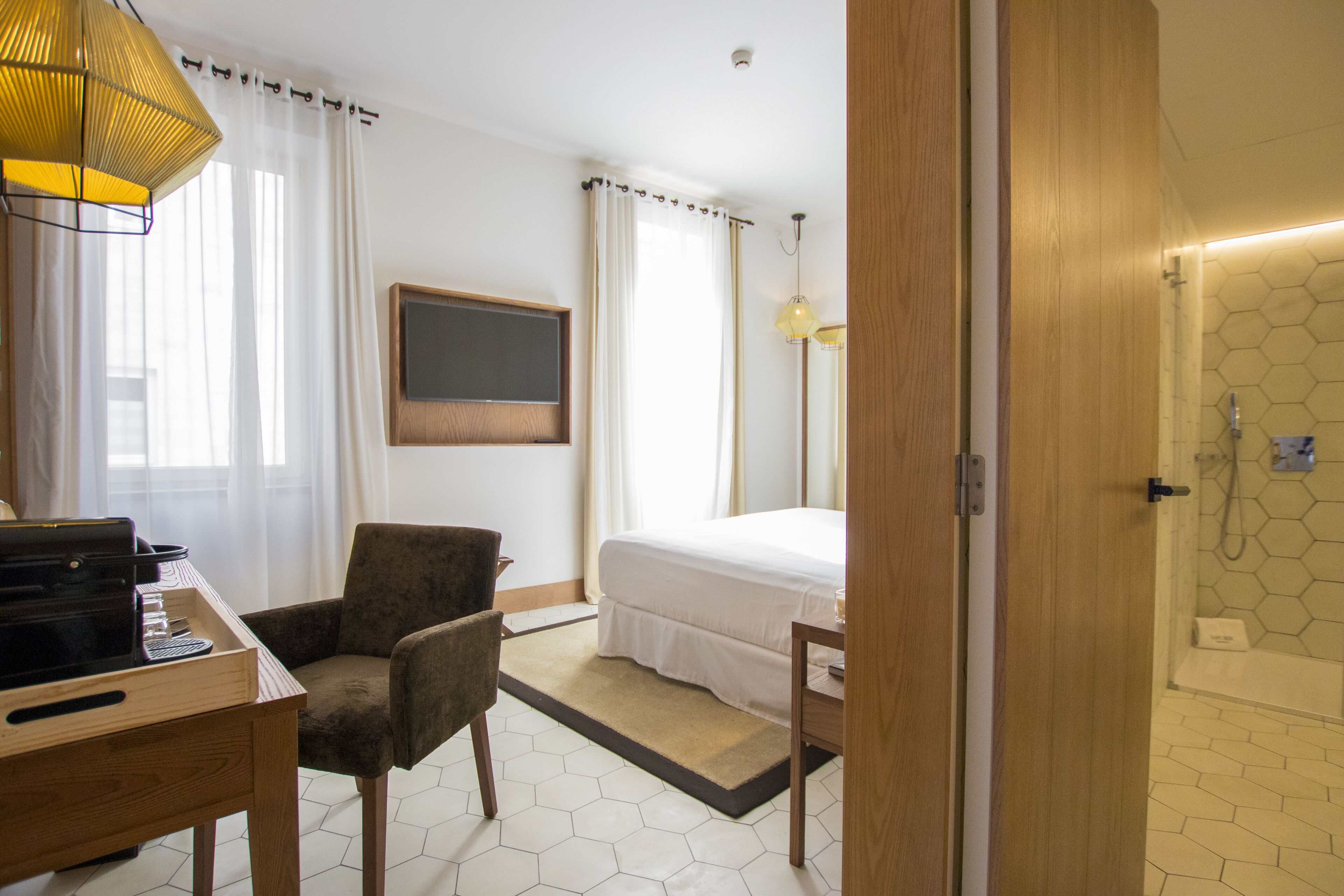 Habitación de hotel con cama, escritorio con teclado, silla, lámpara y zona de ducha.