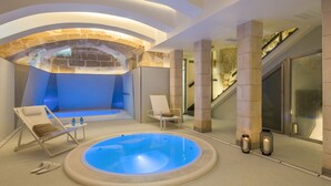 A modern indoor pool area with a hot tub, lounge chairs, and a stone wall backdrop. - Boutique Hotel Sant Roc & Spa (Mahón)