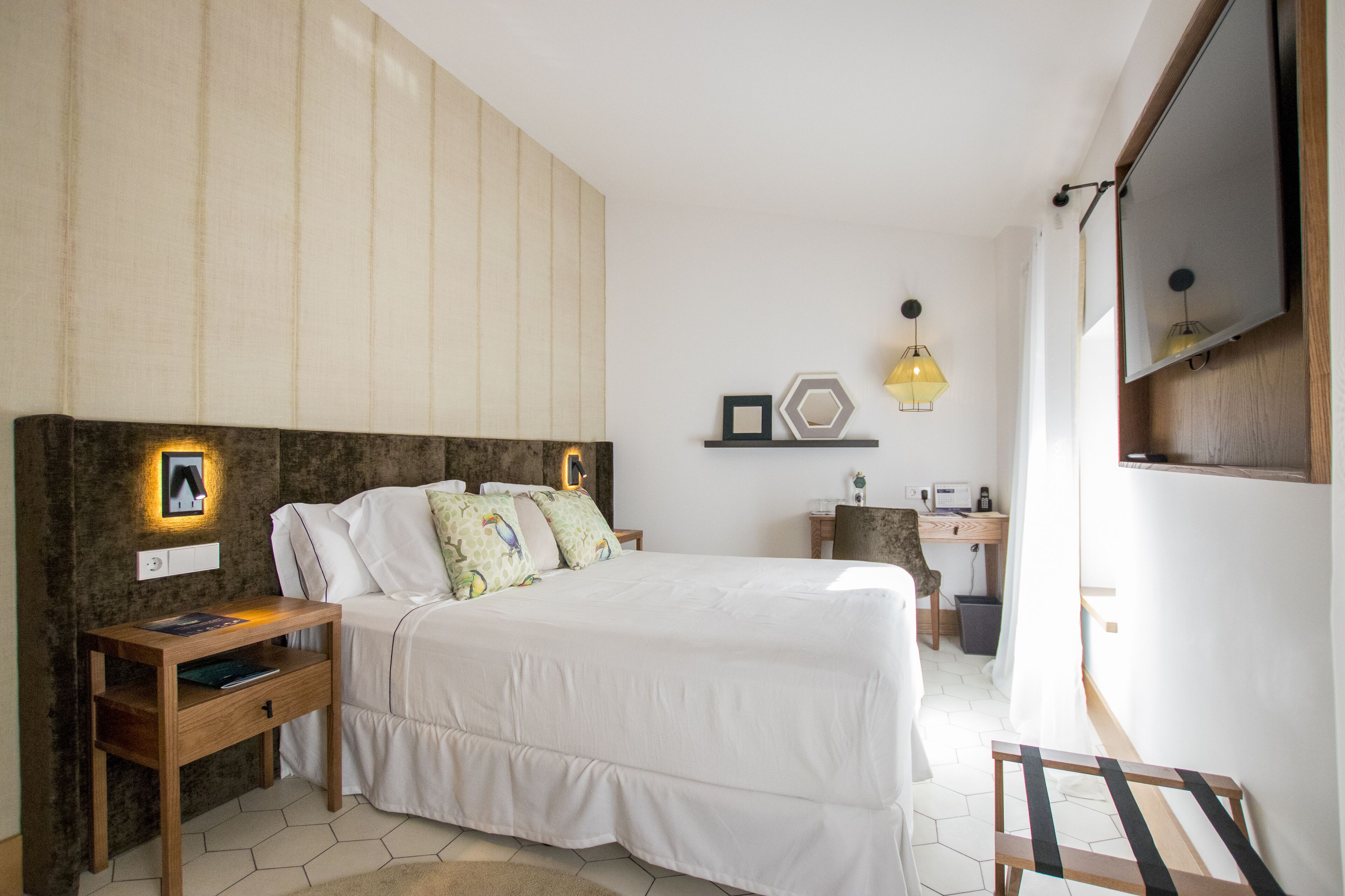 A bedroom with a bed, bedside table, lamp, and a desk with a chair.