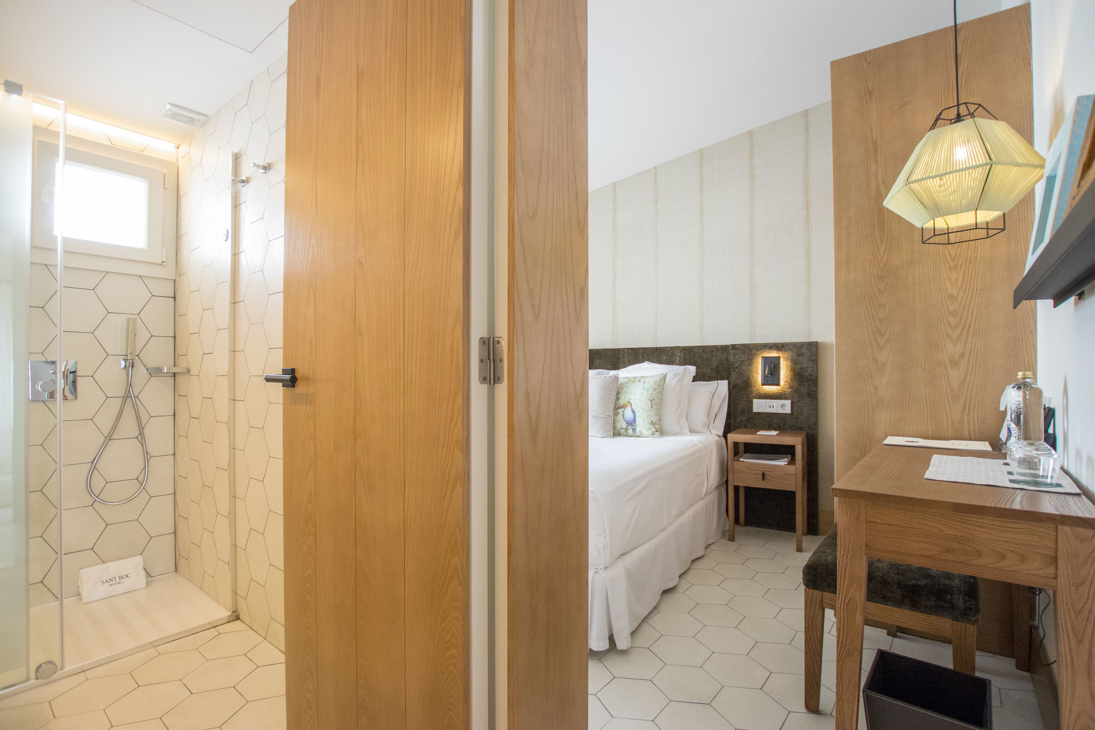 Una habitación de hotel con ducha, cama con ropa blanca, un escritorio de madera y una mesita de noche.