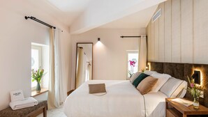 A modern bedroom with a large bed, bedside tables, a bench, and a mirror. - Boutique Hotel Sant Roc & Spa (Mahón)