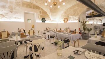 A restaurant with hexagonal tiled floors, white furniture, and a stone wall. Tables are set with plates, cutlery, and napkins.