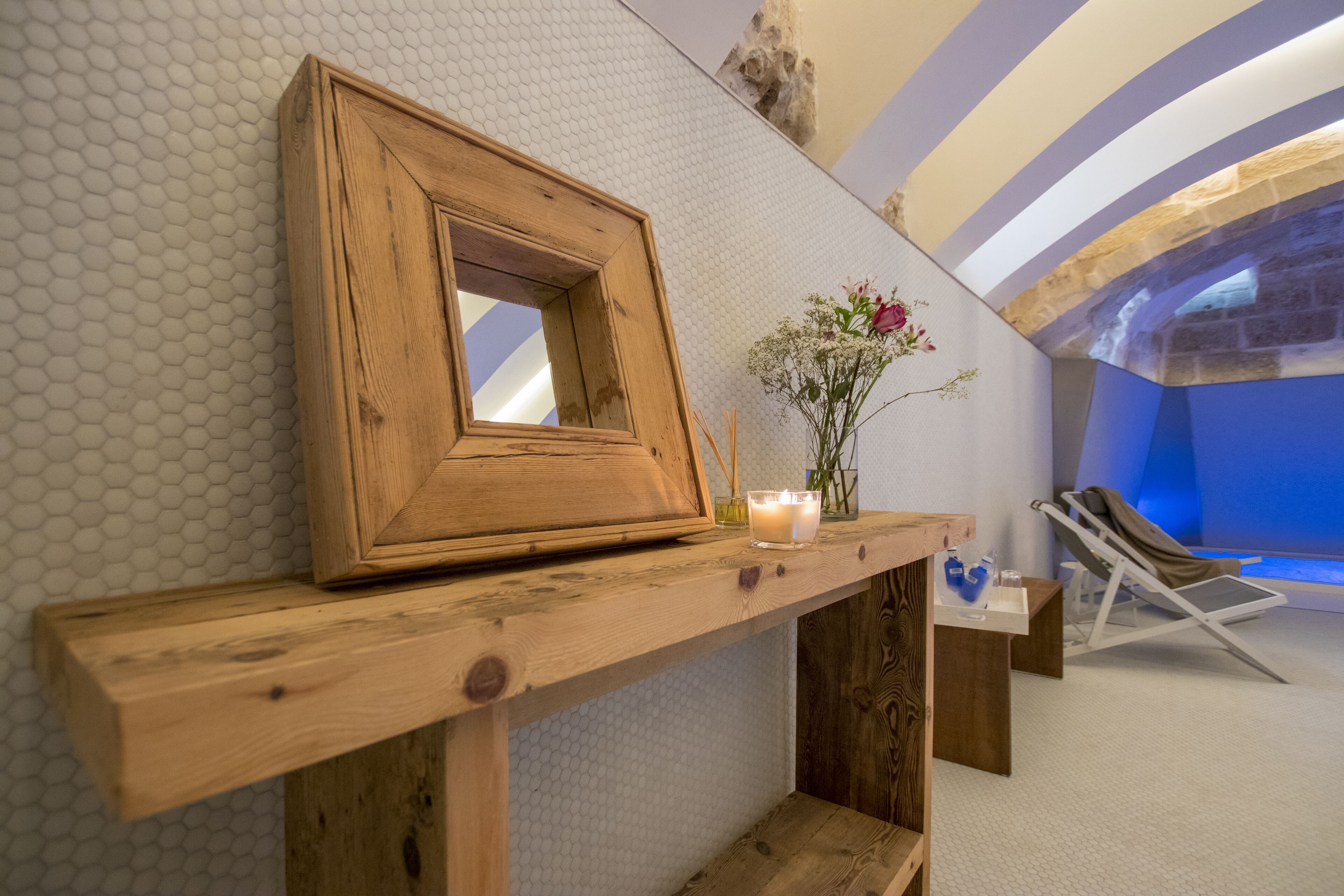 A wooden shelf with a mirror, candles, and a vase of flowers.