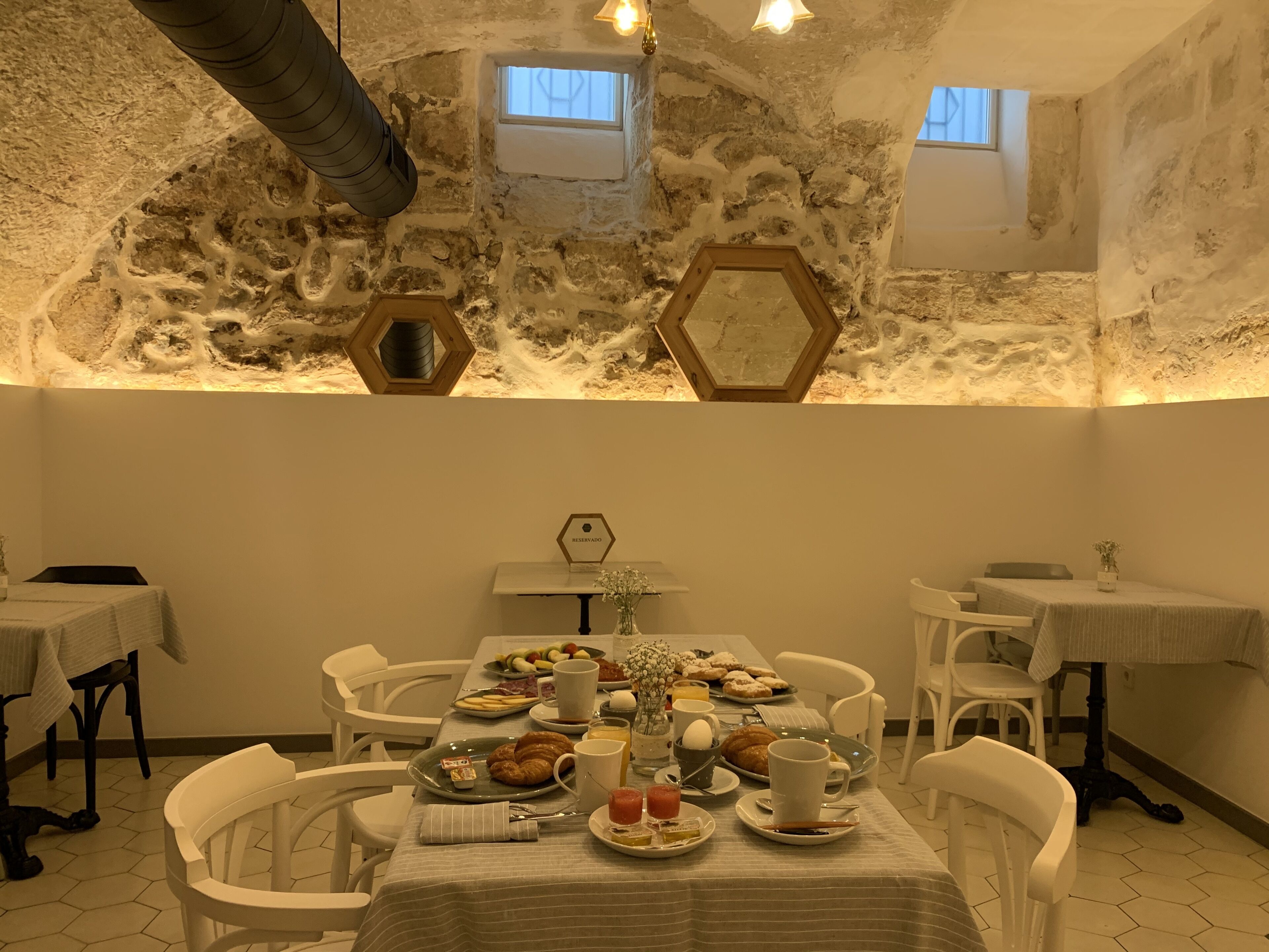 Comedor con paredes de piedra, espejos hexagonales y una mesa dispuesta para el desayuno.