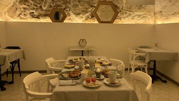 Comedor con paredes de piedra, espejos hexagonales y una mesa dispuesta para el desayuno.