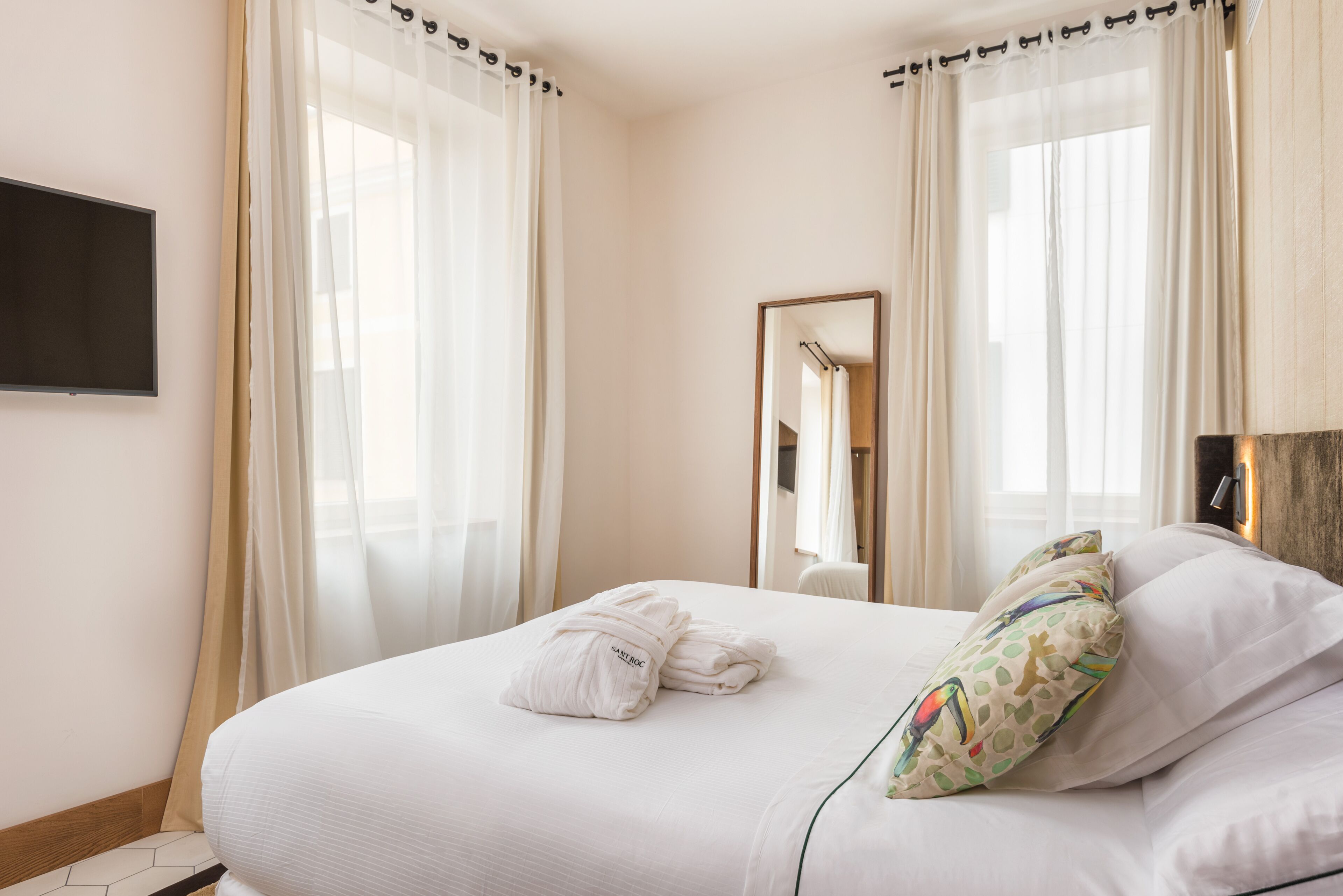Een hotelkamer met een opgemaakt bed, een flatscreen televisie aan de muur en een grote spiegel.