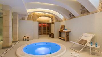 Een spa ruimte met een whirlpool, een lounge stoel en een houten bank.