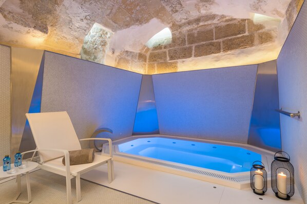 A modern spa room with a hot tub, a lounge chair, and two candles. - Boutique Hotel Sant Roc & Spa (Mahón)