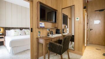 Habitación de hotel con cama, escritorio, silla, televisor y espejo.