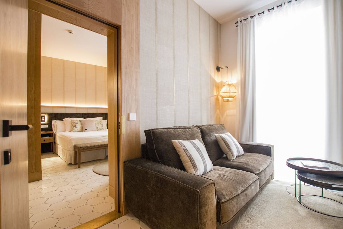 A modern hotel room with a brown sofa, a round coffee table, and a bed with a wooden headboard.