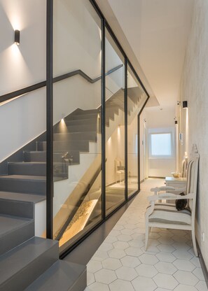 A modern interior with a glass staircase, a seating area with a patterned rug, and a view of the outdoors. - Boutique Hotel Sant Roc & Spa (Mahón)