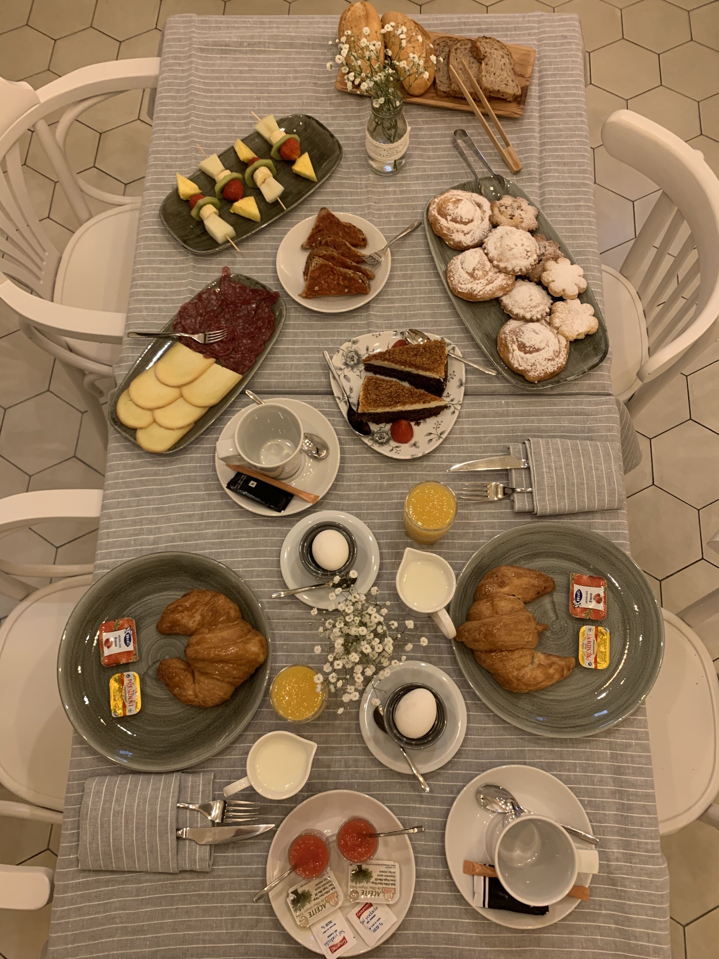 A breakfast table with various food items, including pastries, fruit skewers, and croissants.
