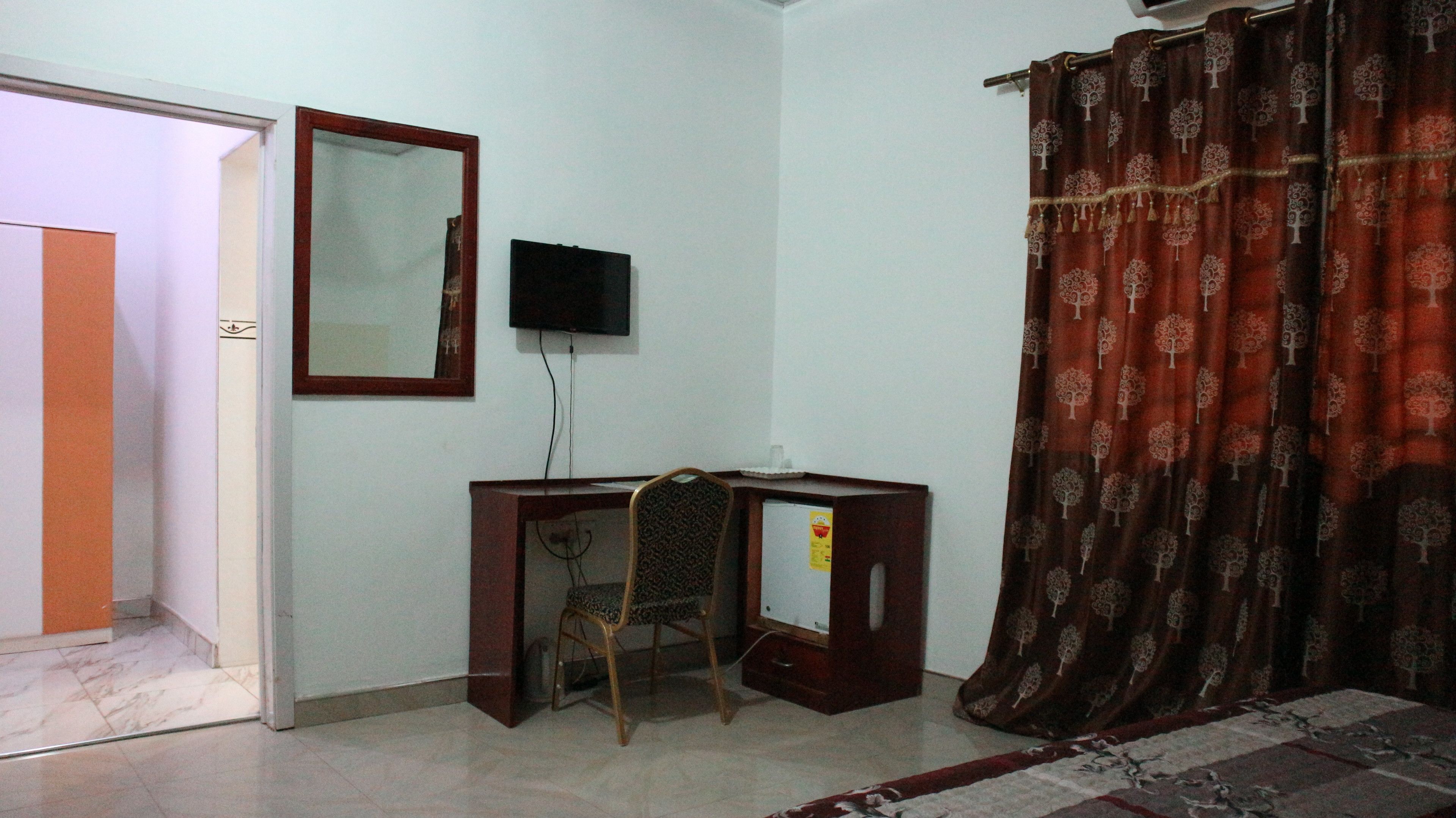 A room with a desk, a chair, a television, and a patterned curtain.