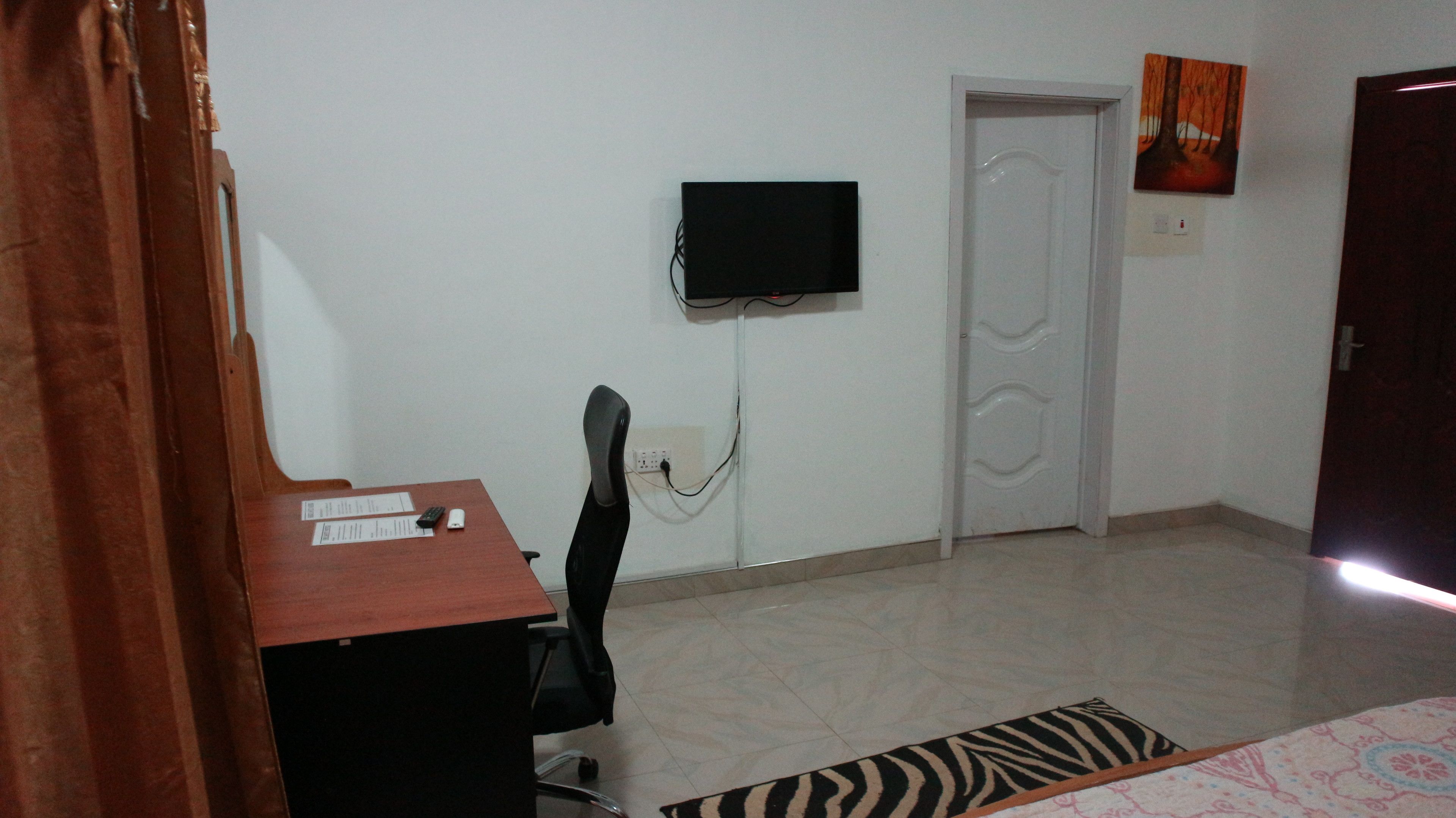 A room with a desk, chair, and a television mounted on the wall.