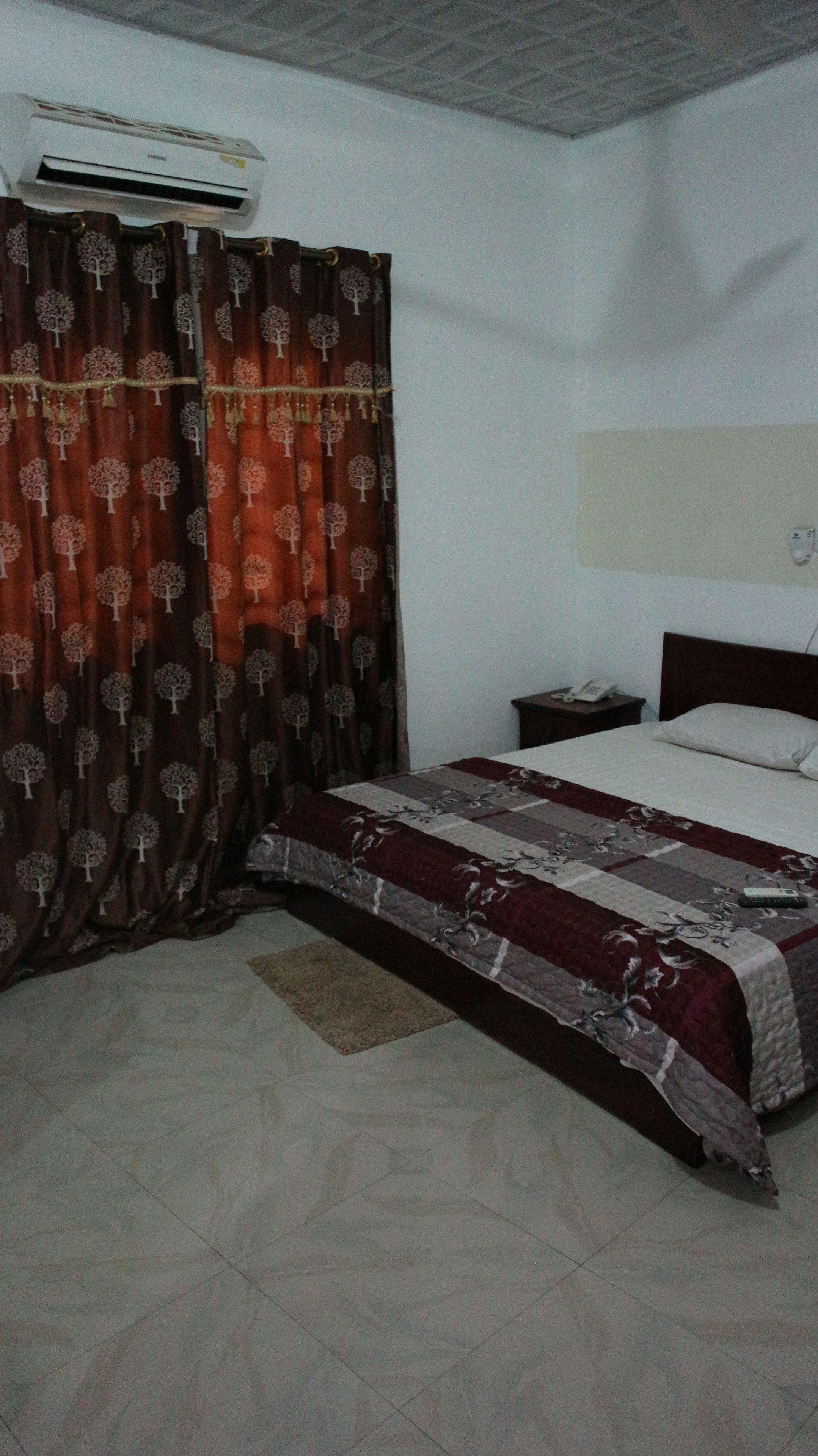 A bedroom with a bed, curtains, a bedside table, and an air conditioning unit.