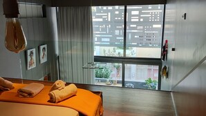 Una habitación de hotel moderna con un ventanal grande, una cama con ropa de cama naranja y una lámpara colgante.