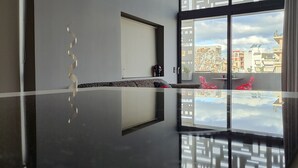 Un interior moderno con suelo reflectante, un sofá, una silla y vistas de la ciudad a través de grandes ventanales.