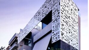 Un edificio moderno de varios pisos con una fachada geométrica distintiva, balcones y un estacionamiento.
