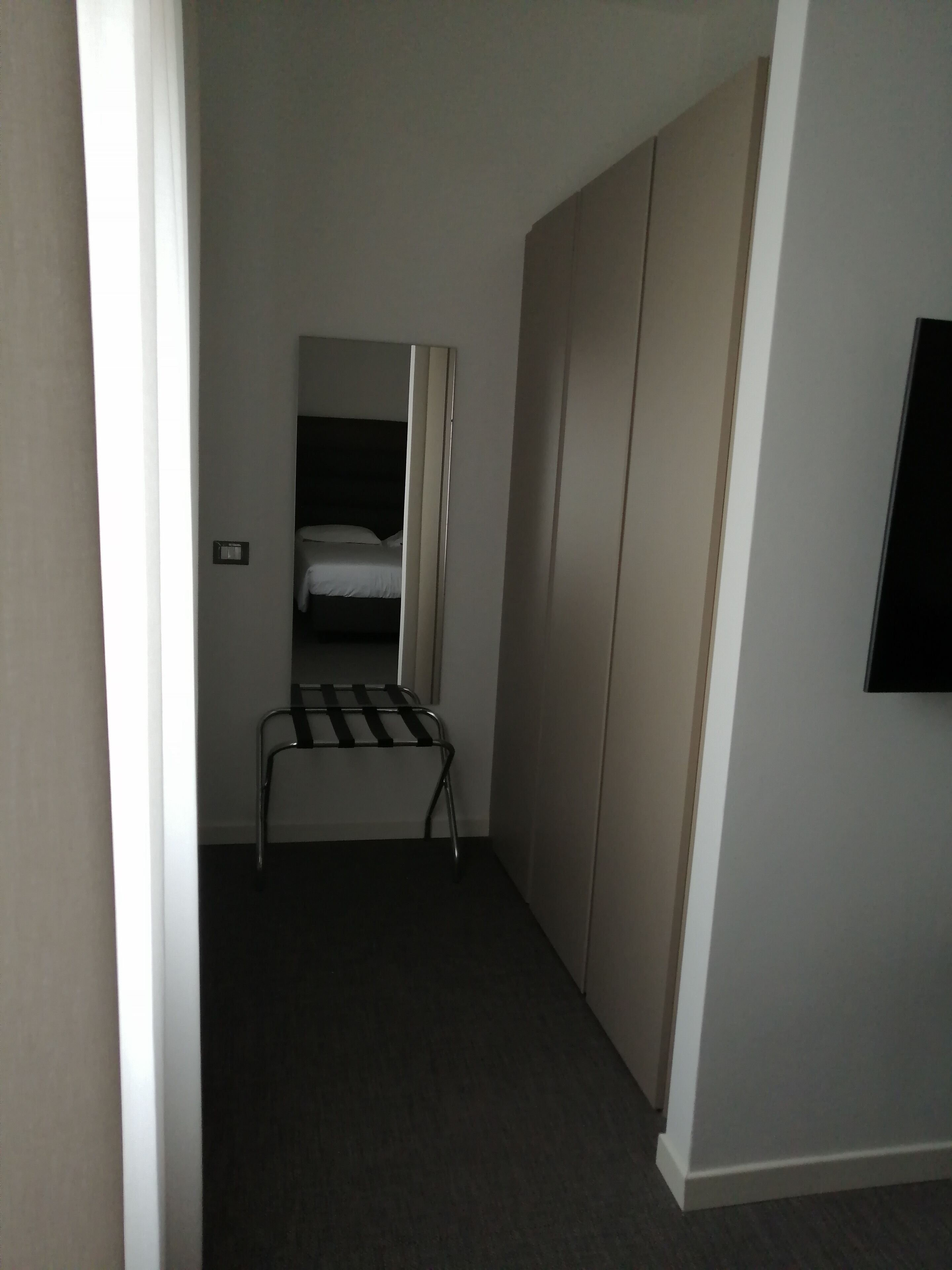 A narrow hallway with a bed in the background, a metal rack, and a wardrobe.