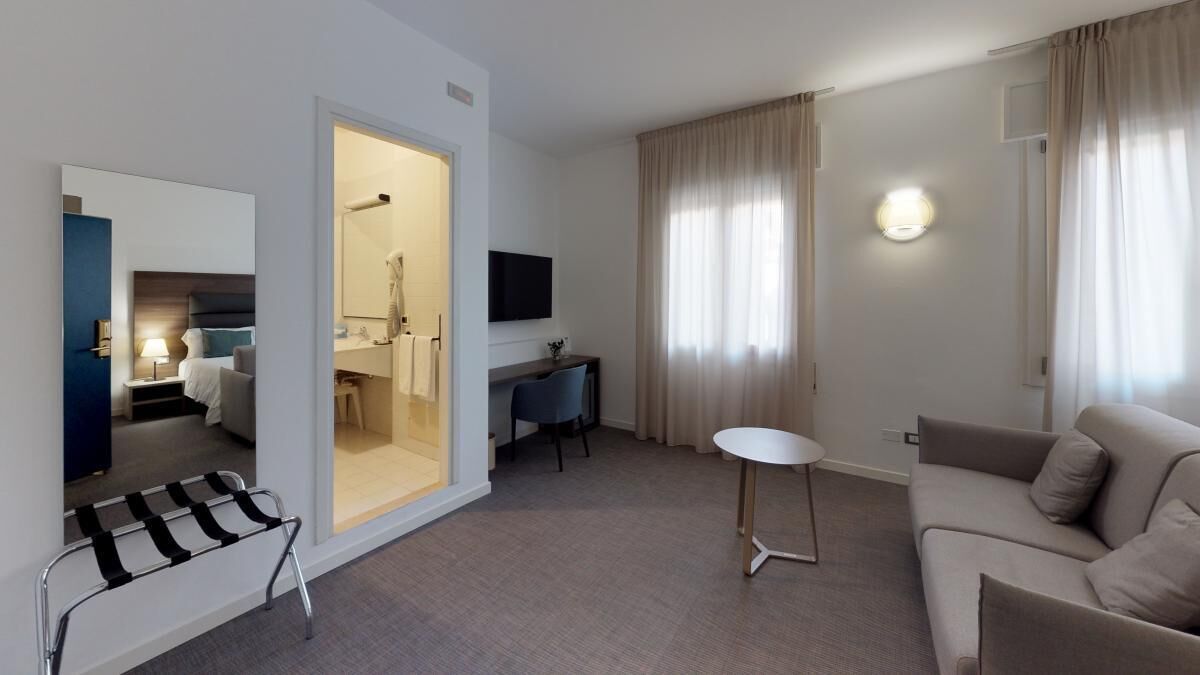 Quarto de hotel moderno com uma cama, uma escrivaninha, uma mesinha e um sofá.