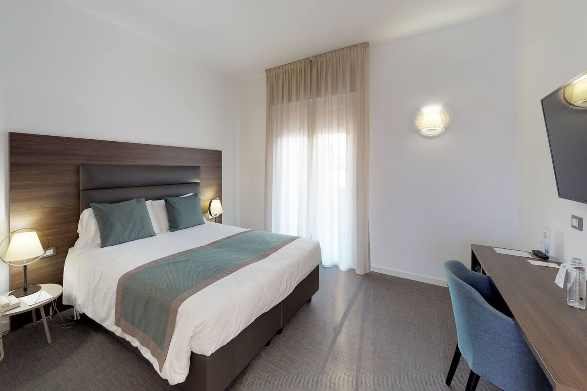 A hotel room with a large bed, bedside lamps, a desk with a chair, and a TV mounted on the wall.