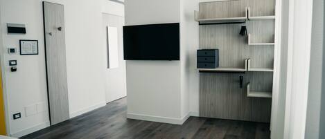 Una habitación de hotel moderna con una cama grande, un televisor de pantalla plana montado en la pared, un armario de madera y una estantería empotrada.