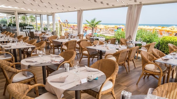 Een restaurant met rieten meubels en gedekte tafels, met uitzicht op een strand.