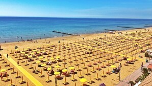 Een strand met rijen ligbedden en parasols, een steiger die het water in loopt, en een heldere lucht.