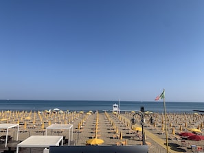 A beach with rows of sunbeds and umbrellas, a lifeguard tower, and a flag.