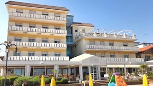 Een hotel met meerdere balkons, een strandgedeelte met parasols, en een bordje met Villa Sorriso erop.