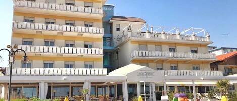 A hotel with multiple balconies, a beach area with umbrellas, and a sign for Villa Sorriso.