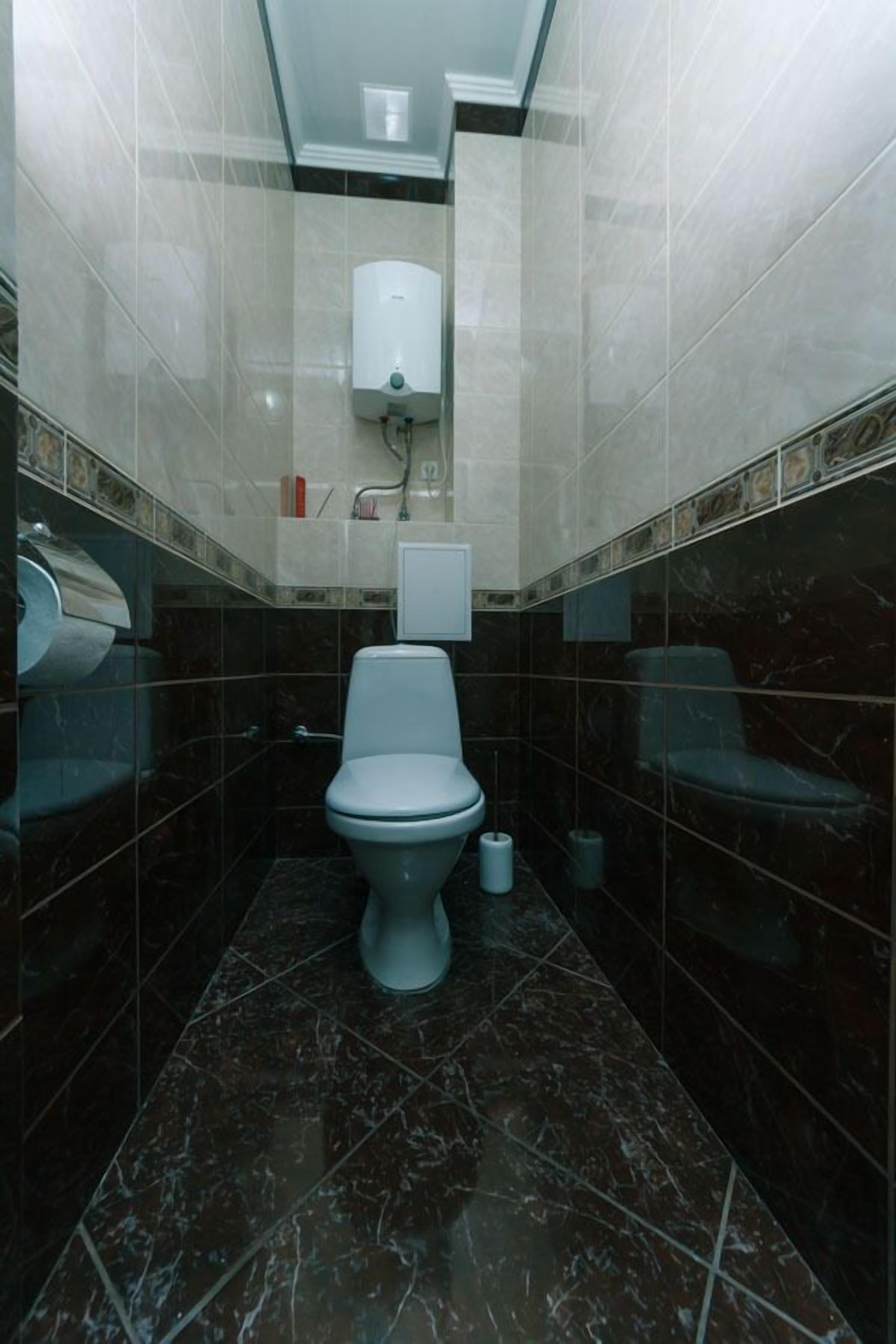 A small, modern bathroom with a toilet, a hand dryer, and a trash bin.