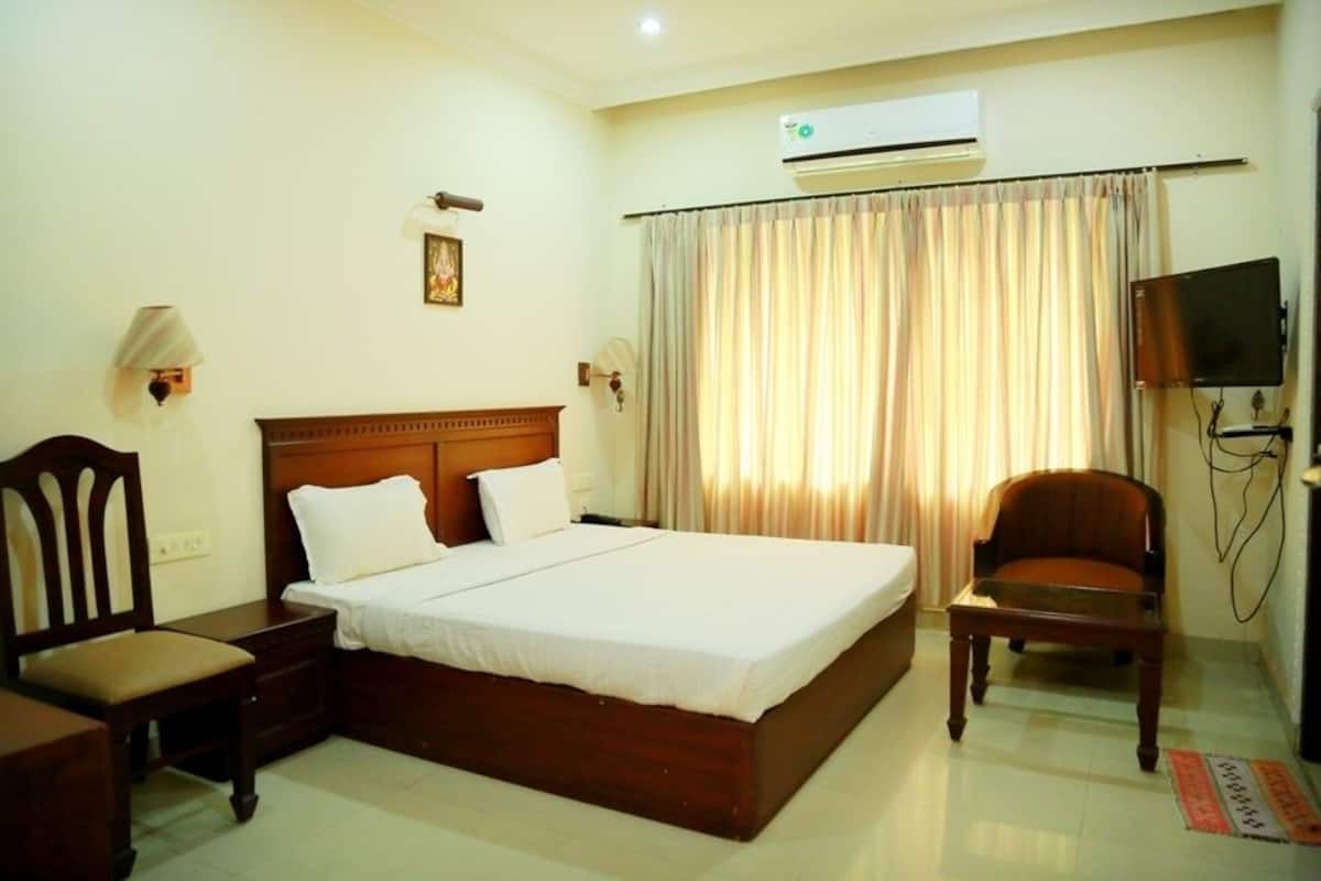 Quarto de hotel com uma cama grande, mesa de cabeceira de madeira, uma cadeira, televisão e ar condicionado.
