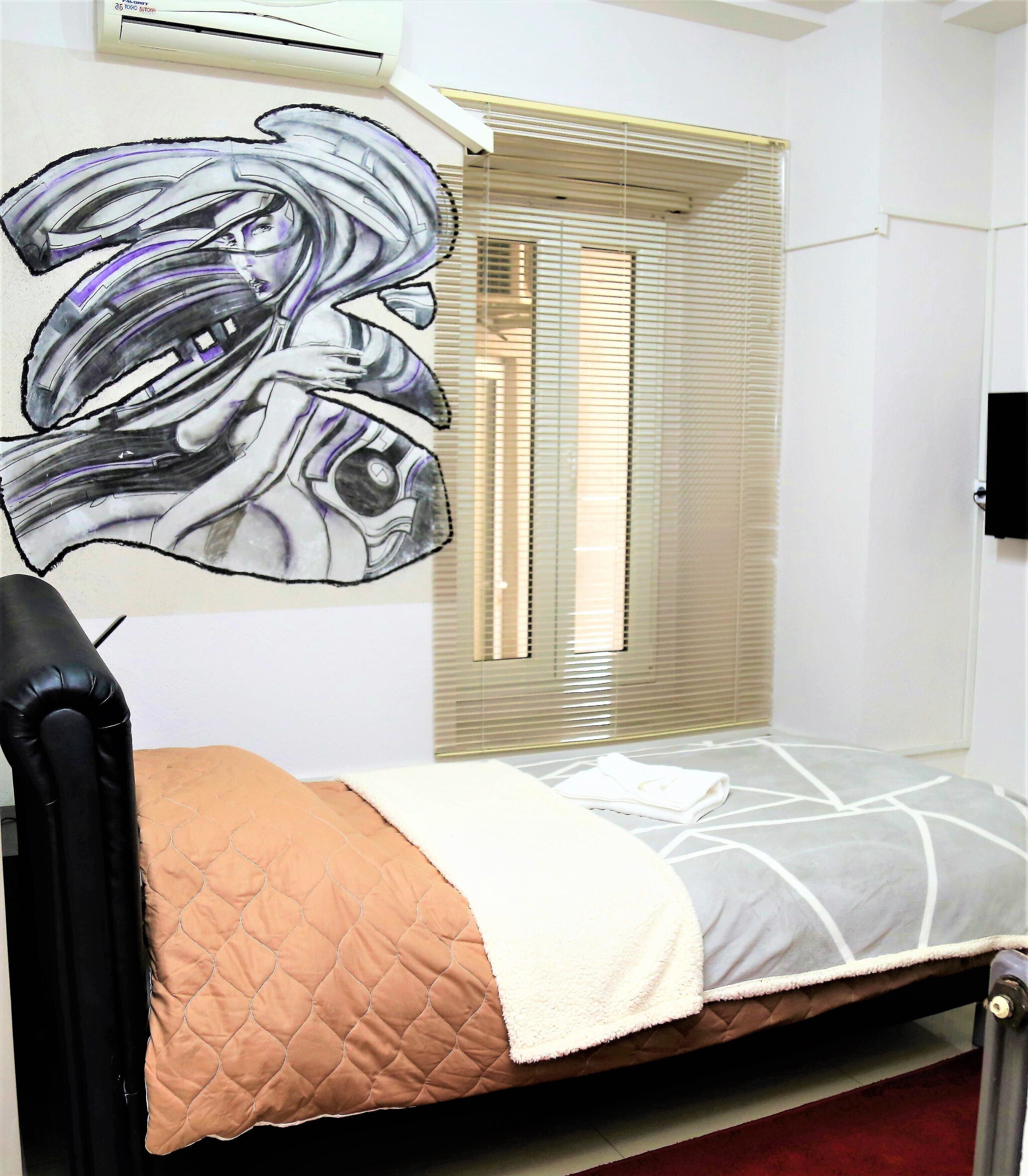 A room with a bed, a window with blinds, and a wall-mounted air conditioner.