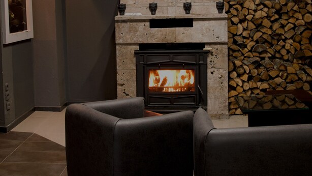 A modern living room with a stone fireplace, a stack of firewood, and leather sofas.