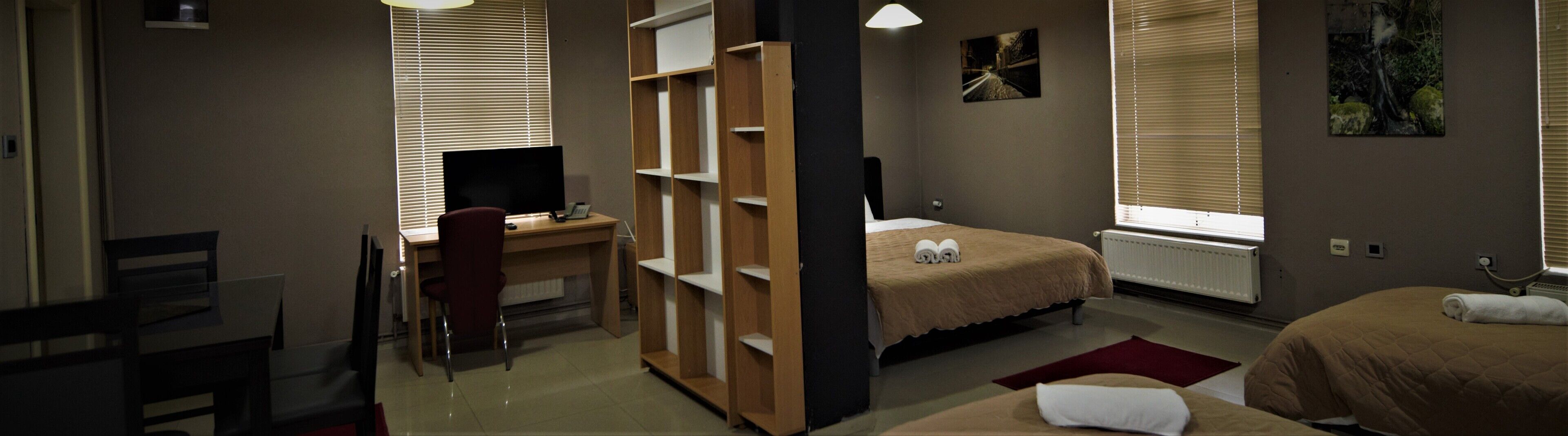 A bedroom with a desk, a bed, and a window with blinds.