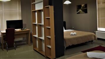 A bedroom with a desk, a bed, and a window with blinds.