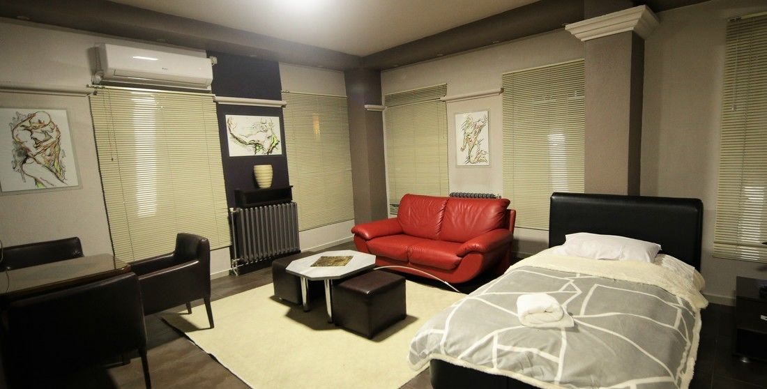 Habitación de hotel con una cama, un sofá de cuero rojo, una mesita, un escritorio y obras de arte en las paredes.