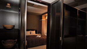 A modern hotel room with a bed, a wooden bowl on a shelf, and a dark wardrobe.
