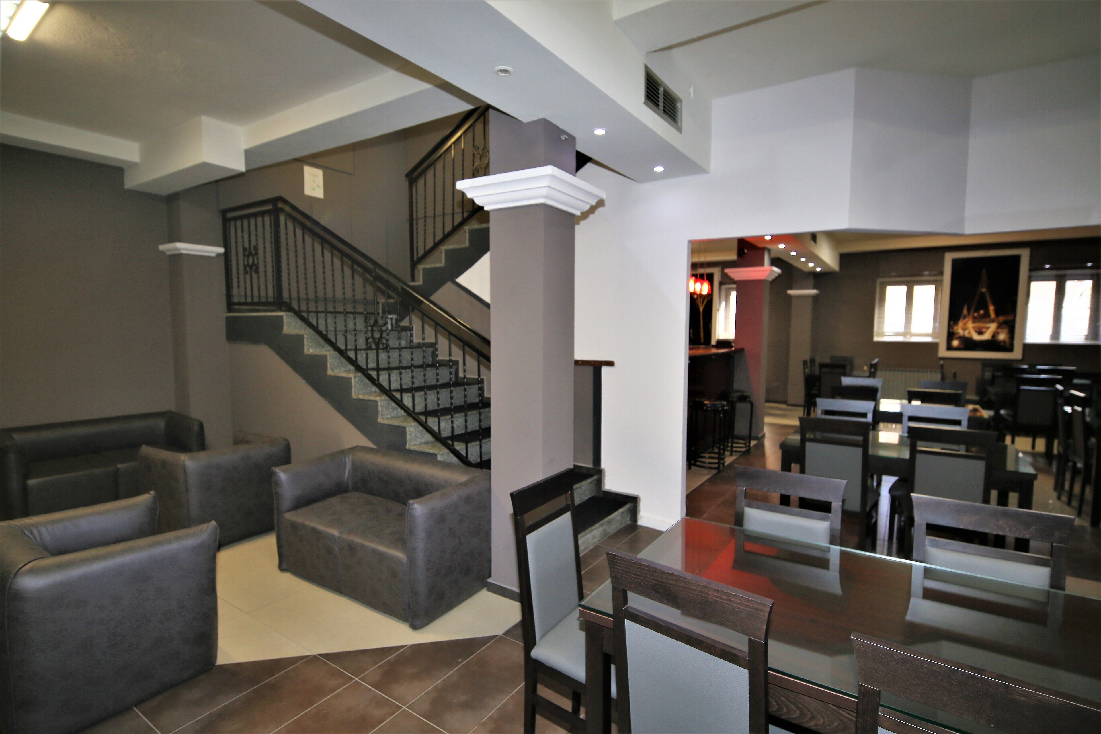 A spacious living area with a staircase, leather sofas, and a dining area with glass-top tables and chairs.