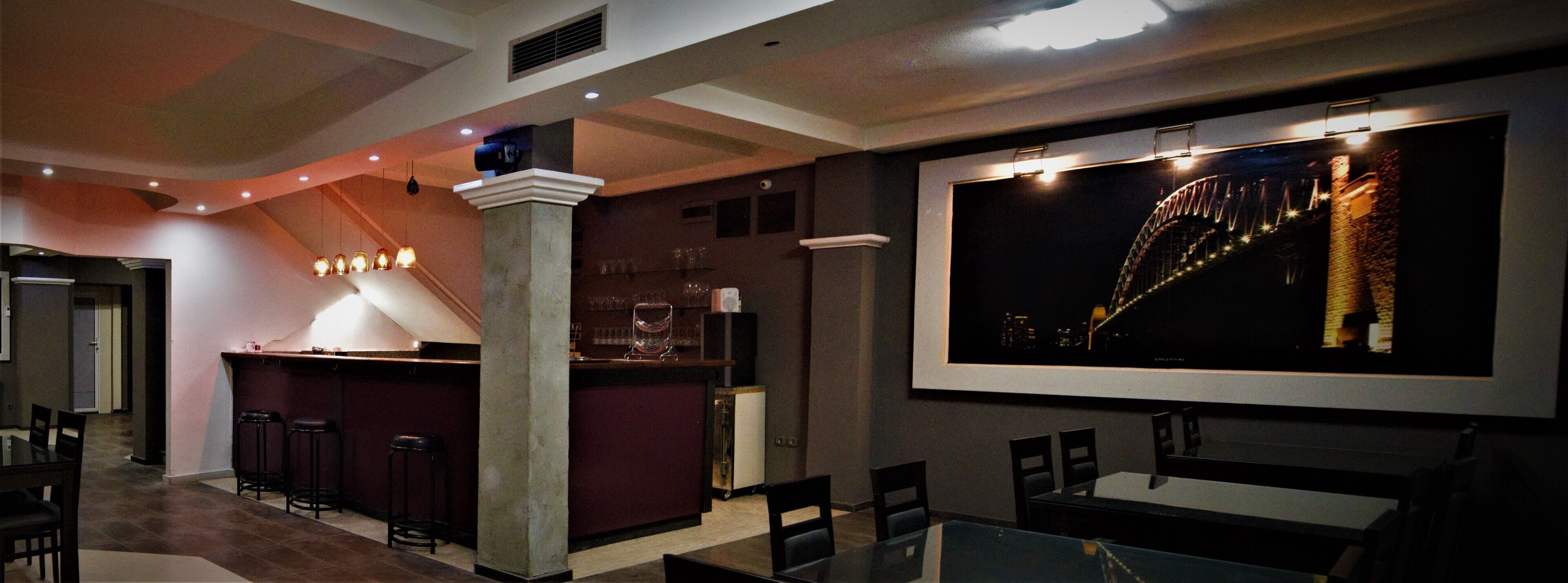 A bar area with stools, a counter, and a large screen displaying a bridge.