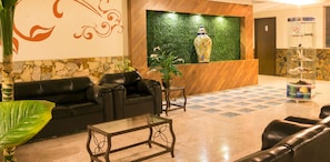 A lobby with a reception desk, a black leather sofa, a glass coffee table, and a decorative vase.