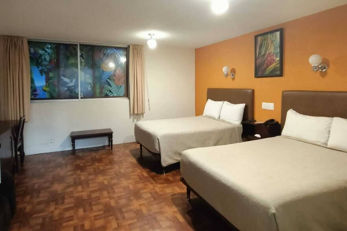 Habitación de hotel con dos camas, un banco, un escritorio, una silla y una ventana con cortinas.