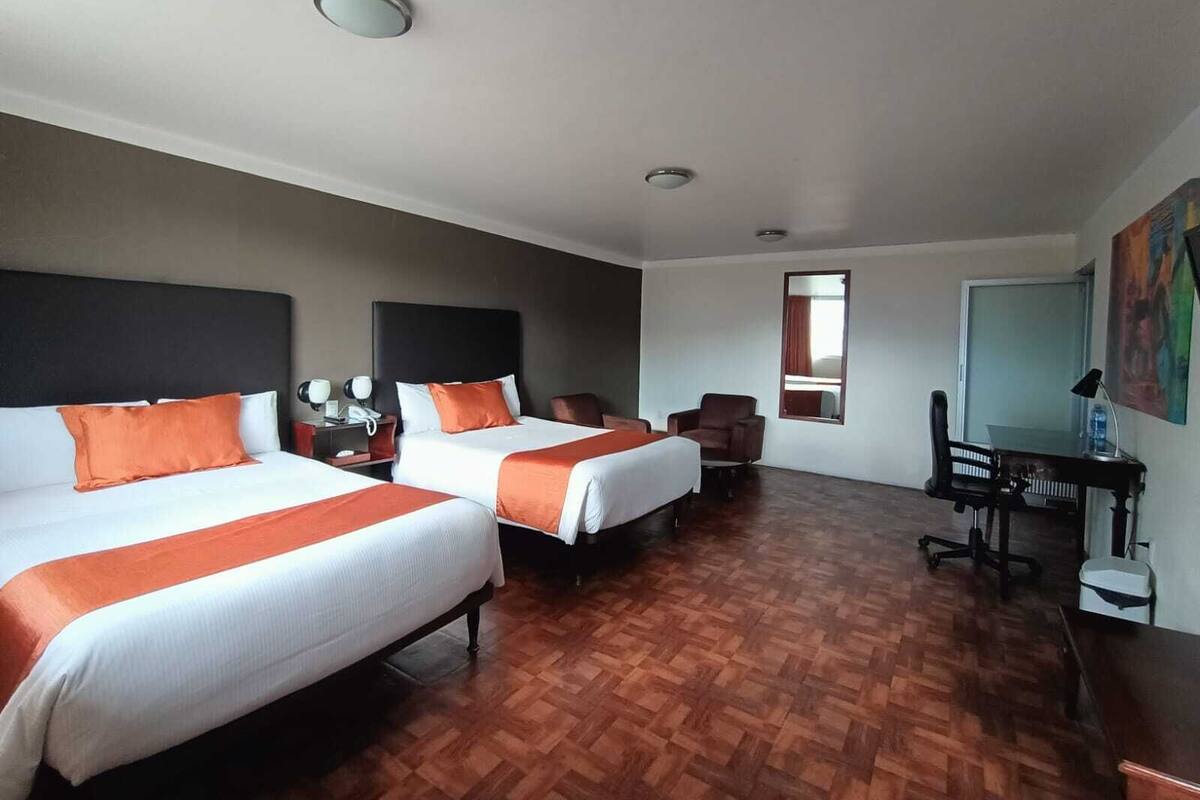 Una habitación de hotel con dos camas, un escritorio, una silla y una mesita.