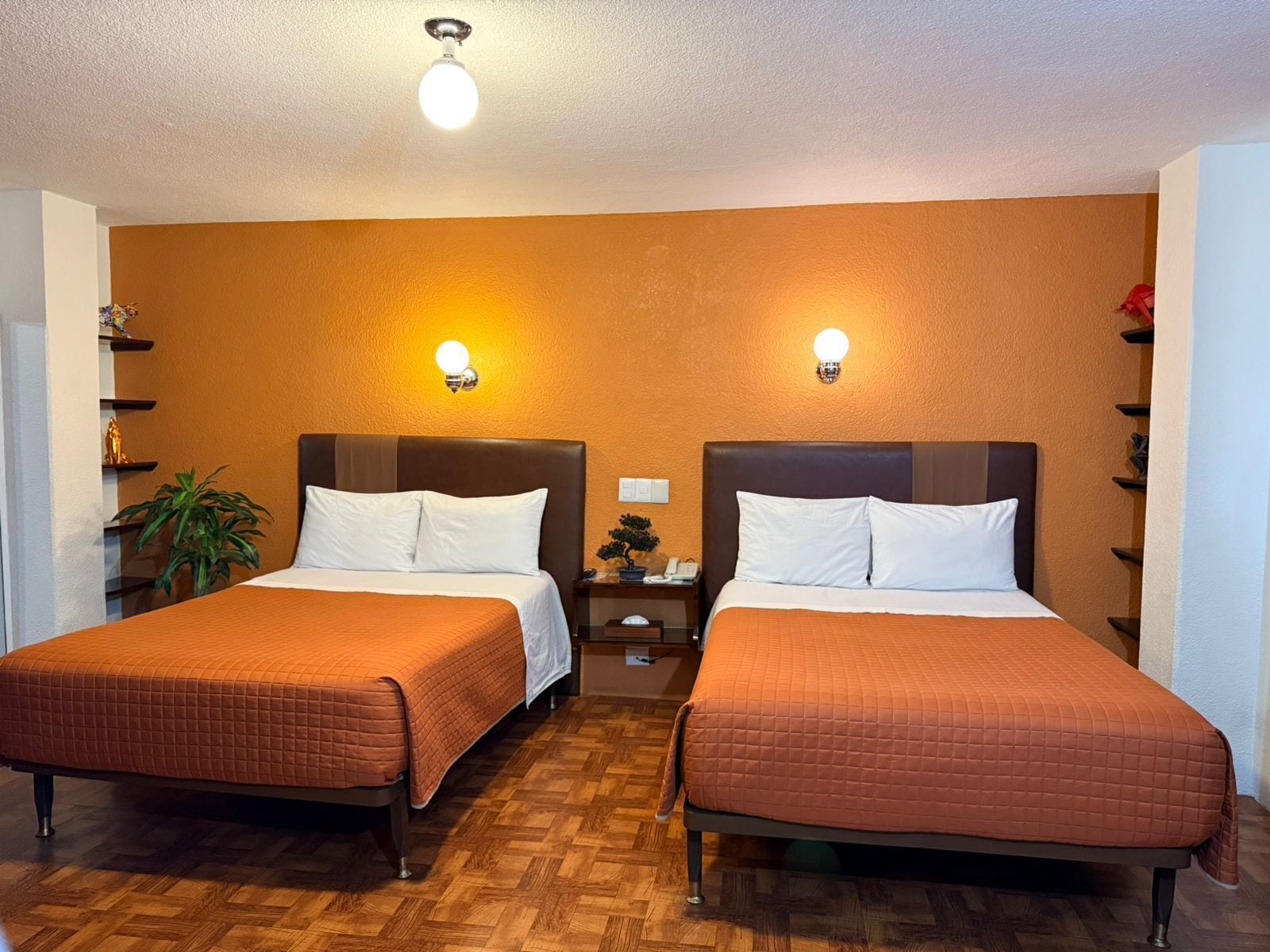 A hotel room with two beds, wooden flooring, and wall-mounted light fixtures.