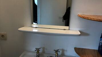 A bathroom with a white sink, a mirror above it, and a shelf with a bag of tissues.