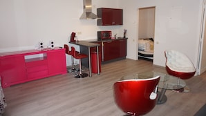 A modern kitchen with red cabinetry, a microwave, and a red bar stool. There is a glass table with a red chair in the foreground. - Domaine Les Hochets (Vresse-sur-Semois)