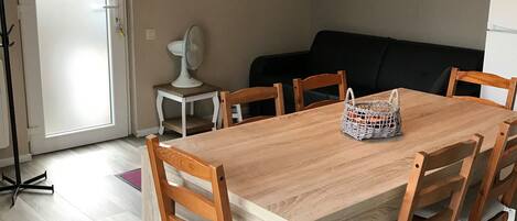 A dining area with a wooden table and chairs, a small white fan, and a framed picture on the wall.
