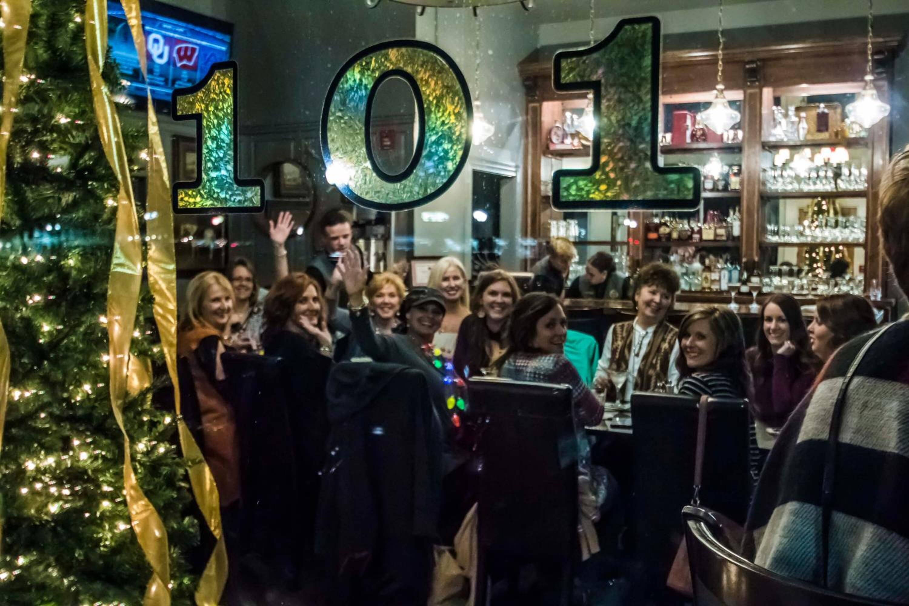 A group of people gathered around a bar area with a Christmas tree and festive decorations.