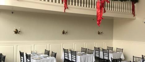 A dining area with multiple tables set for service, white walls, and a chandelier.
